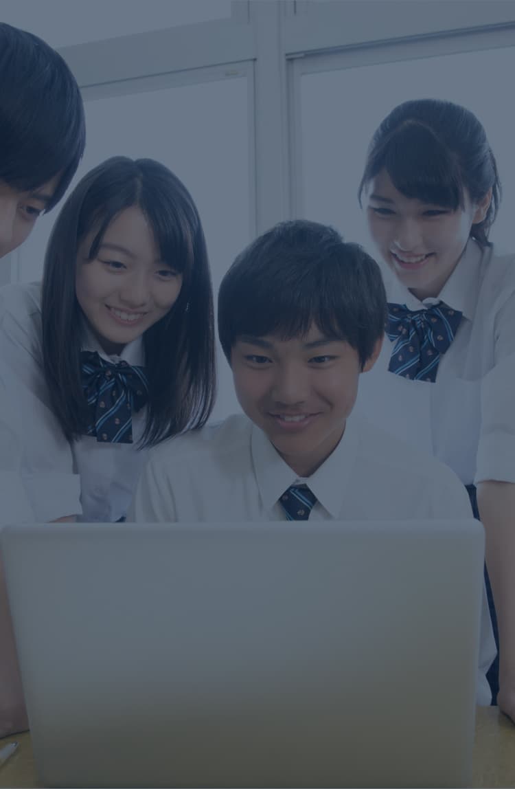 教室で先生が授業を進め、生徒がノートパソコンで学習する様子。大きなディスプレイには学習動画が表示されている。